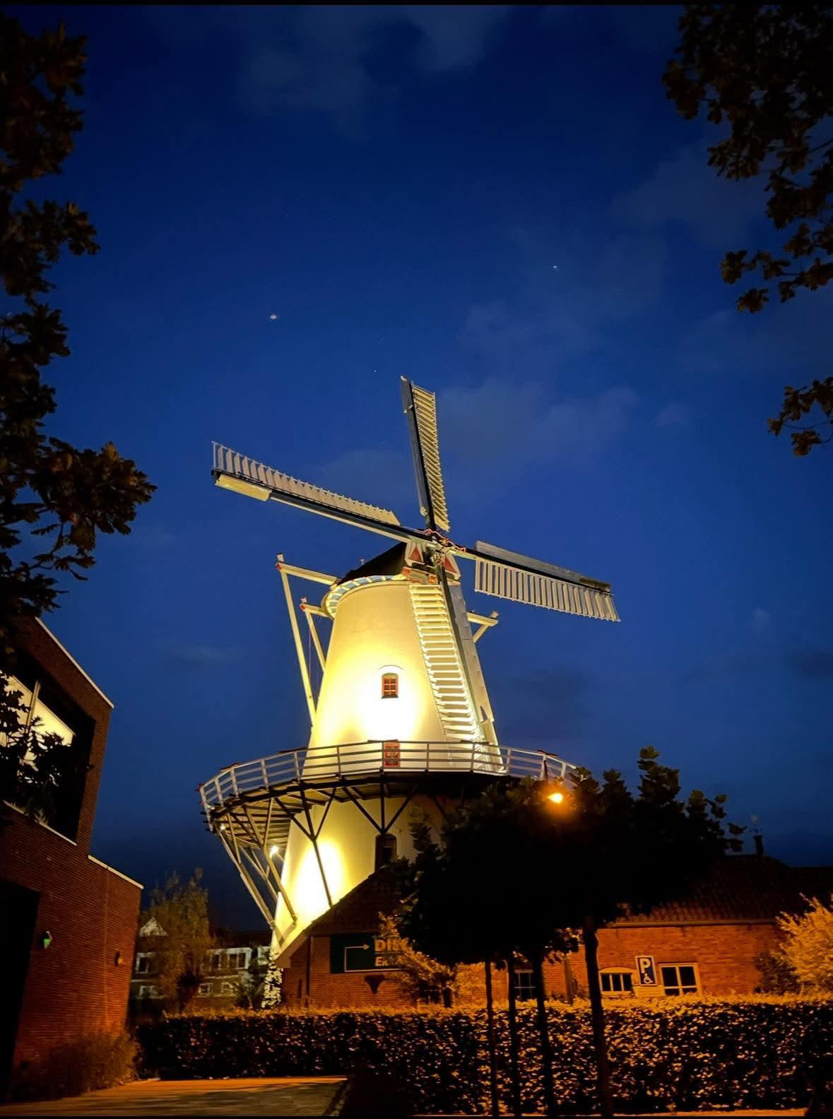 De verlichte Molen De Hoop onder een diepblauwe avondlucht.